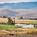 Union, OR 15 Rolling hills golf course with a small pond, two golf carts, and scattered houses in the distance, set against a backdrop of mountains and cloudy sky. Grassy and dry areas blend throughout the landscape.