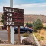 Union, OR 16 A wooden sign reads Buffalo Peak Golf Course 1224 E. Fulton with a red outline of a buffalo, set in a parking lot with a car and hills in the background.